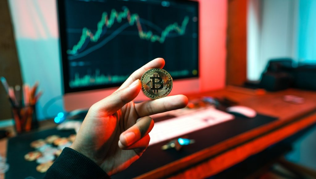 Młody człowiek trzyma w ręku monetę Bitcoin, znaną jako BTC.